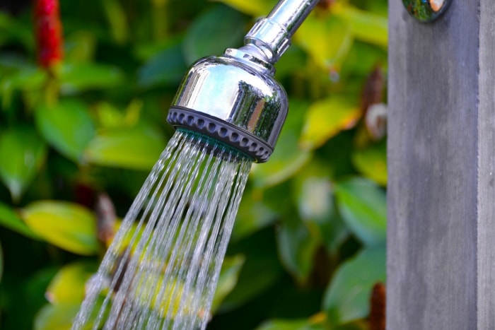 Gros plan sur la meilleure option de douche extérieure pulvérisant de l'eau avec une grande plante à l'arrière-plan.