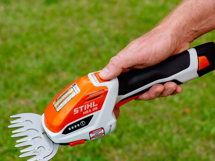 Gros plan du pouce d'un homme sur l'interrupteur de sécurité de la cisaille de jardin sans fil Stihl.