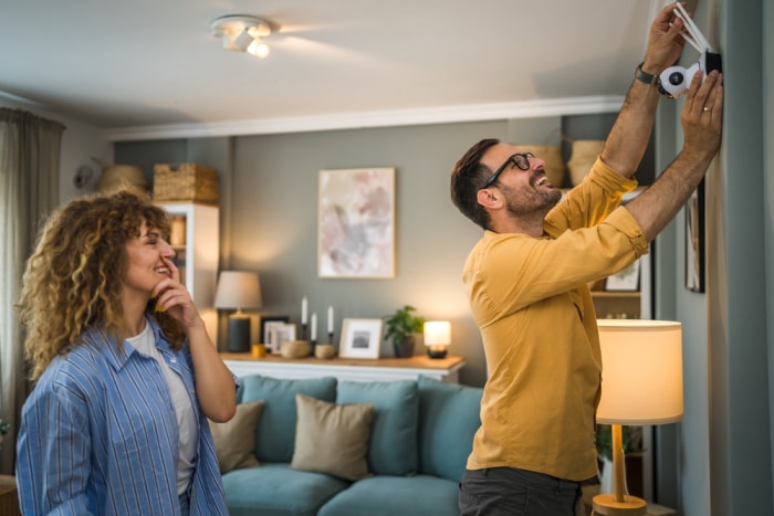 Un homme et une femme installent un système de sécurité domestique dans un salon.