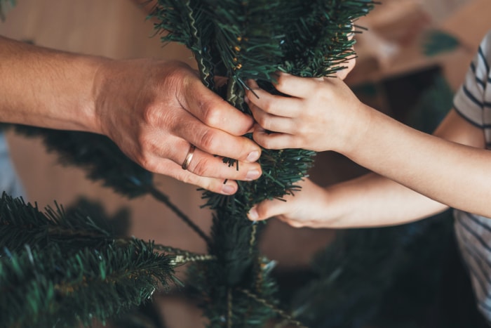 Gros plan sur les mains du père et du fils qui tentent d'assembler l'arbre de Noël artificiel.