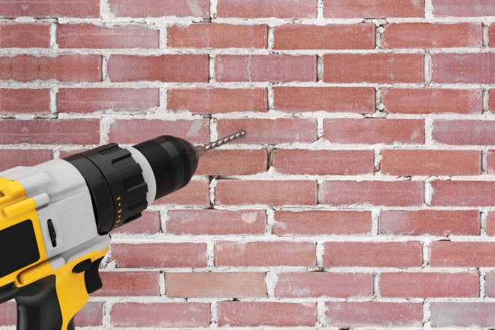 Une perceuse jaune utilisée pour percer un trou dans un mur de briques.