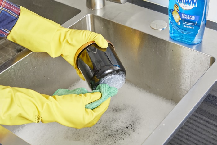 Une femme utilise du savon à vaisselle et de l'eau chaude pour retirer l'autocollant du pot.