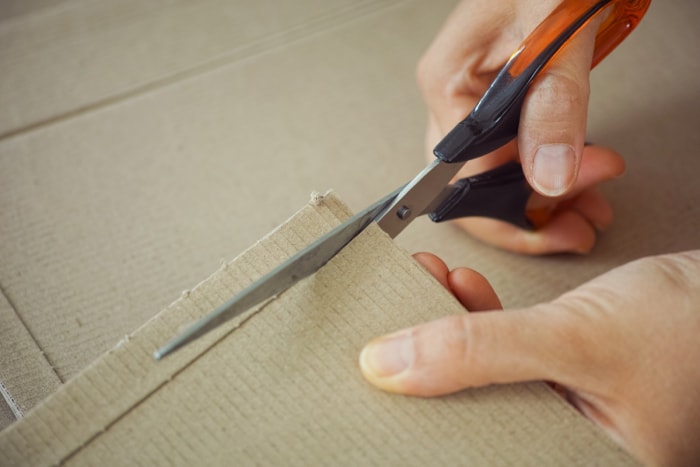 Mains utilisant des ciseaux pour couper du carton.