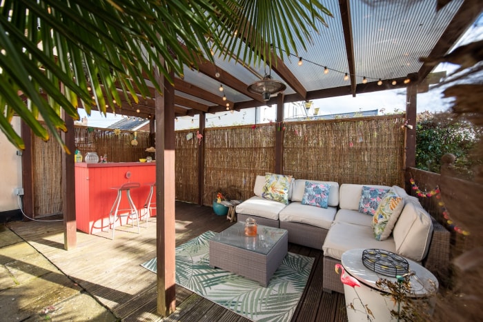 A backyard cabana with patio furniture and a red tiki bar.