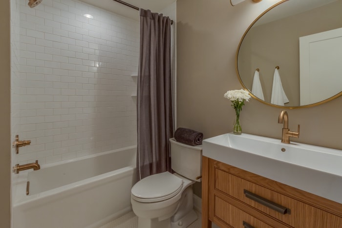 Salle de bains complète avec douche et baignoire combinées blanches et miroir circulaire doré.