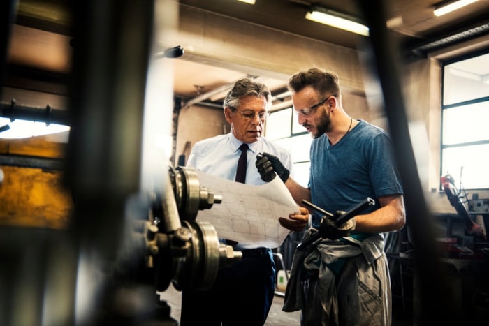 Un homme en cravate et un soudeur regardent un plan de bâtiment.