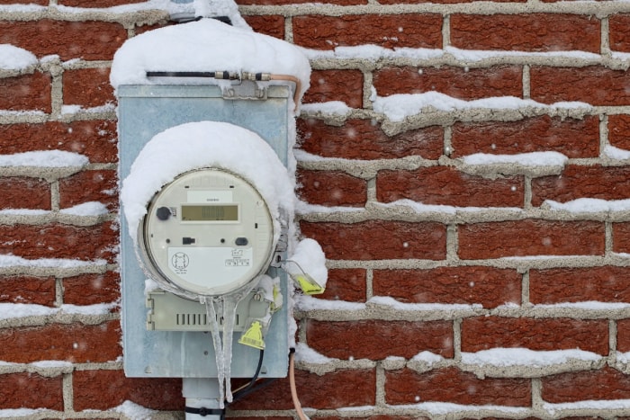 Un compteur électrique domestique à l'extérieur d'un extérieur en briques avec de la neige dessus.