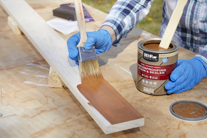 Une femme applique une teinture brune et un scellant pour imperméabiliser une planche de bois.