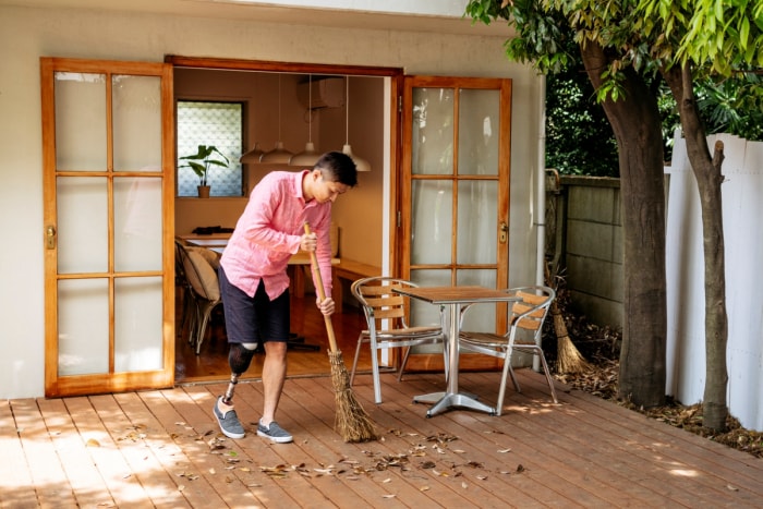 Un homme balaie une terrasse en bois avec un balai.