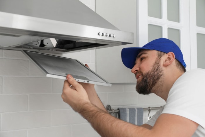 Combien coûte l'installation d'une hotte de cuisine : coût de l'installation d'une hotte de cuisine Un électricien professionnel installe une nouvelle hotte de cuisine dans une cuisine moderne.