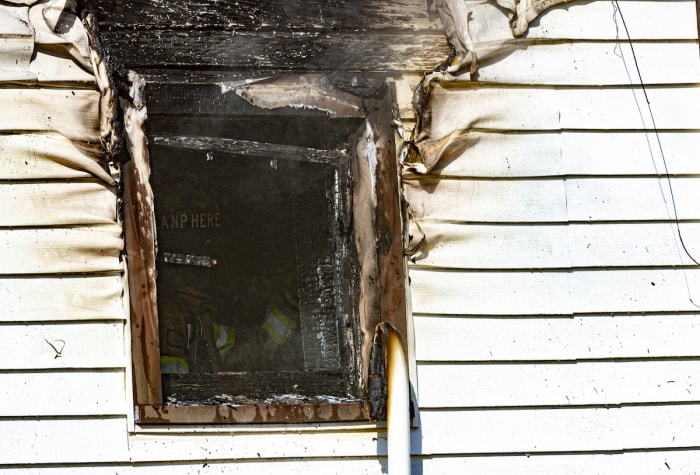 Le bardage et la fenêtre d'une maison blanche sont endommagés par un incendie qui a été éteint par les pompiers dans la fenêtre.