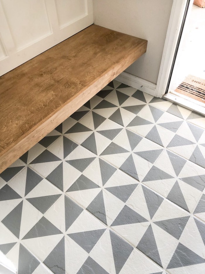 Carrelage géométrique gris dans une entrée avec un banc en bois naturel.