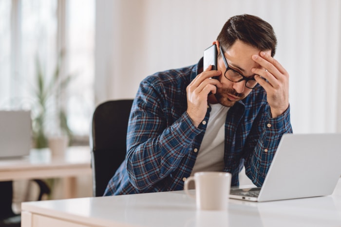 Un locataire impatient est assis à son bureau sur son téléphone portable, attendant de pouvoir joindre quelqu'un.