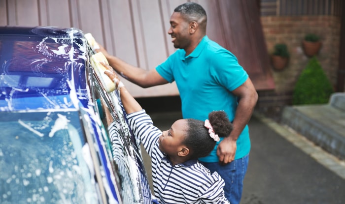 Prise de vue d'un père et de sa fille en train de laver leur voiture à l'extérieur