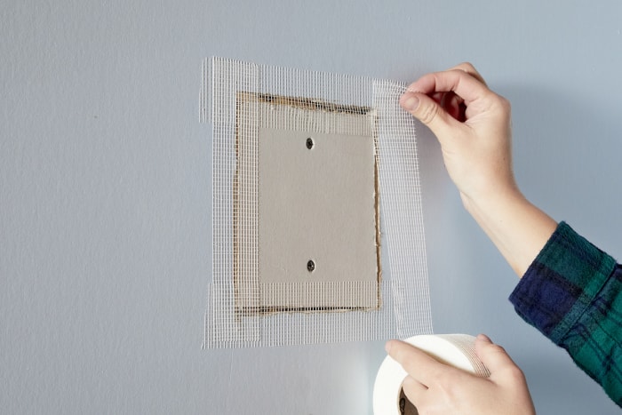 Une femme colle les bords d'une plaque de plâtre avec du ruban adhésif pour cloison sèche.