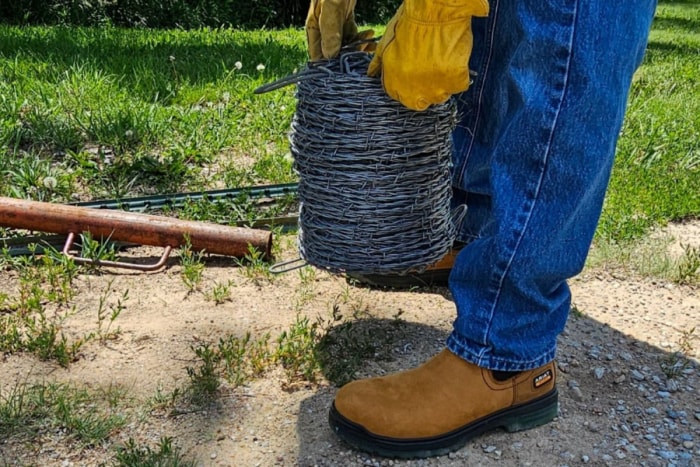 Personne portant des bottes de travail jaunes et des gants de travail jaunes tenant du fil barbelé