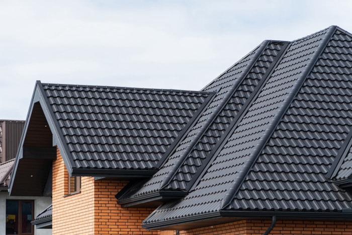 Une maison en briques rouges avec un toit en métal noir façonné en forme de bardeaux. 