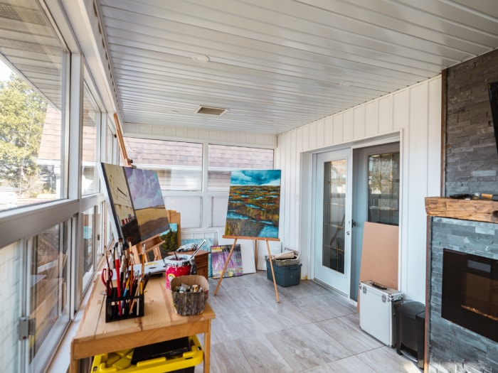 Atelier d'art à domicile sur le porche de la maison avec chevalets, toiles et matériel organisé.