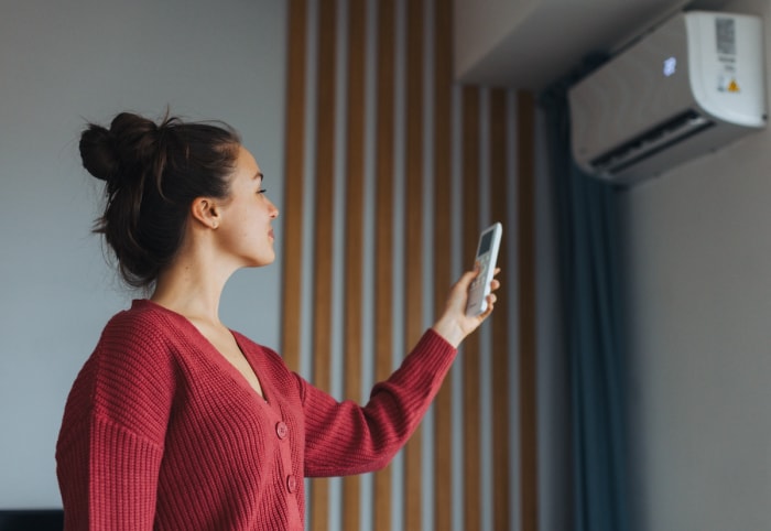 Une jeune femme portant un pull rouge modifie les paramètres de chauffage, de ventilation et de climatisation de sa maison à l'aide d'une télécommande.