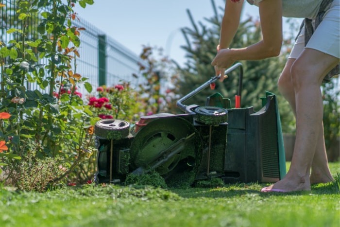 Une personne inspecte une tondeuse à gazon posée sur le sol, sur le côté.