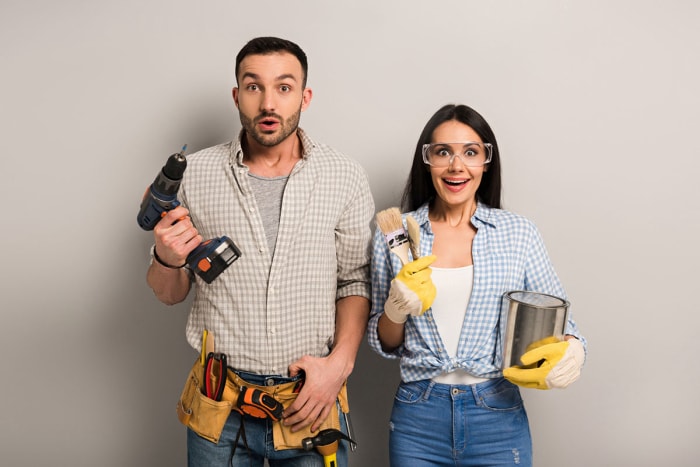 Two people hold up home improvement tools. 