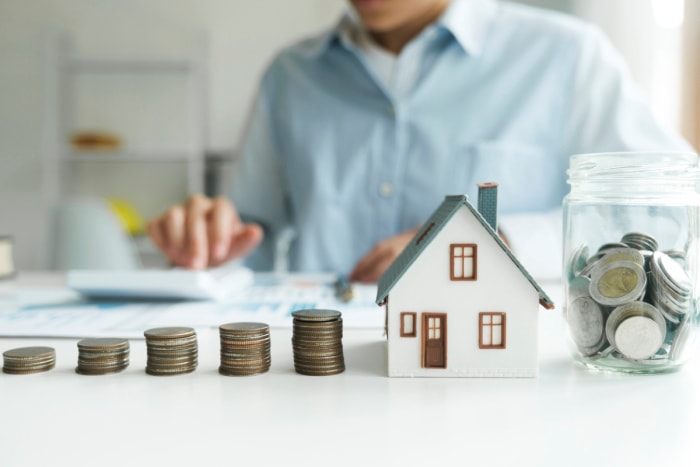 Pièces empilées avec une maison modèle et un pot de pièces sur la table.