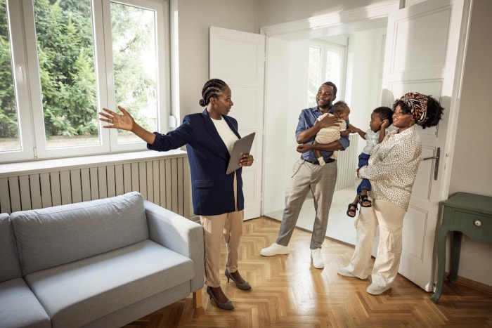 Agent immobilier montrant une maison ouverte à un jeune couple avec un bébé et un jeune enfant. 