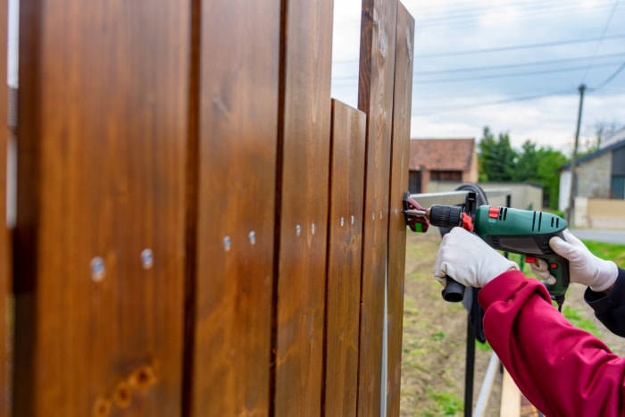 Une personne utilisant une perceuse pour construire une clôture.