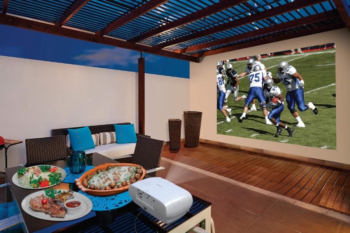 Le meilleur projecteur home cinéma installé sous une pergola et projetant un match de football contre un mur de la terrasse.