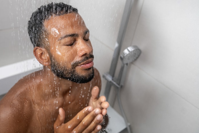 Un homme aux yeux fermés prend une douche avec le visage dans l'eau.