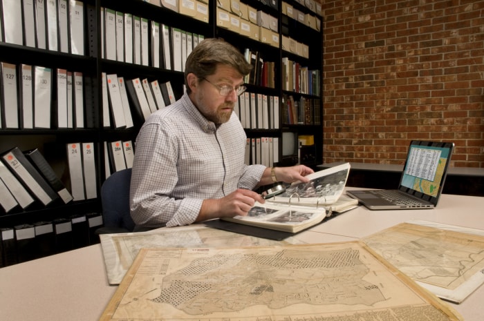 Chercheur dans les archives, examinant des cartes et des photographies.