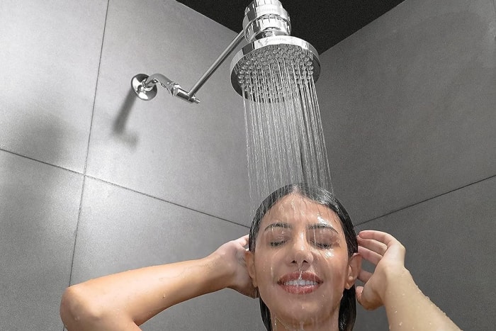 Une personne utilisant la pomme de douche à effet pluie de pointe pour offrir une expérience de douche luxueuse et revigorante