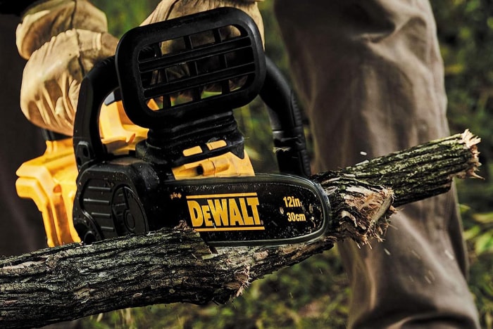 Une personne utilisant la meilleure tronçonneuse sans fil DeWalt pour couper une longueur de branche d'arbre