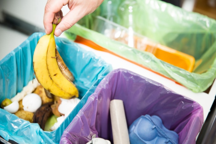 vue aérienne rapprochée des poubelles et du recyclage dans le tiroir de la cuisine avec la main jetant la peau de banane