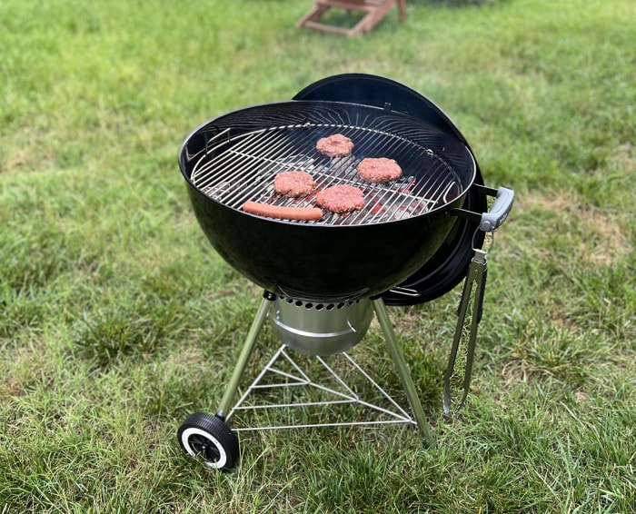 Le barbecue au charbon de bois Weber Original Kettle Premium en cours d'utilisation pour griller de la viande dans une cour