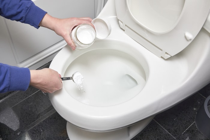 Une femme verse un nettoyant pour cuvette de toilettes à base de bicarbonate de soude dans les toilettes.