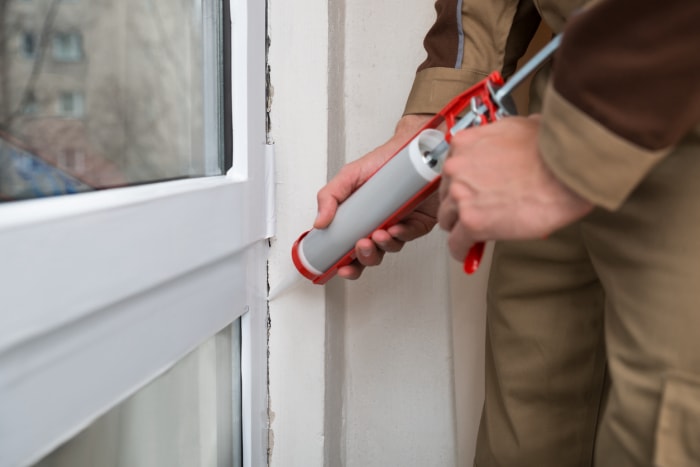 Propriétaire appliquant du mastic silicone avec un pistolet à calfeutrer sur une porte résistante aux intempéries.