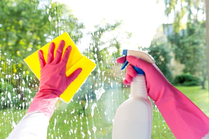 Mains gantées nettoyant la fenêtre avec une serviette jaune