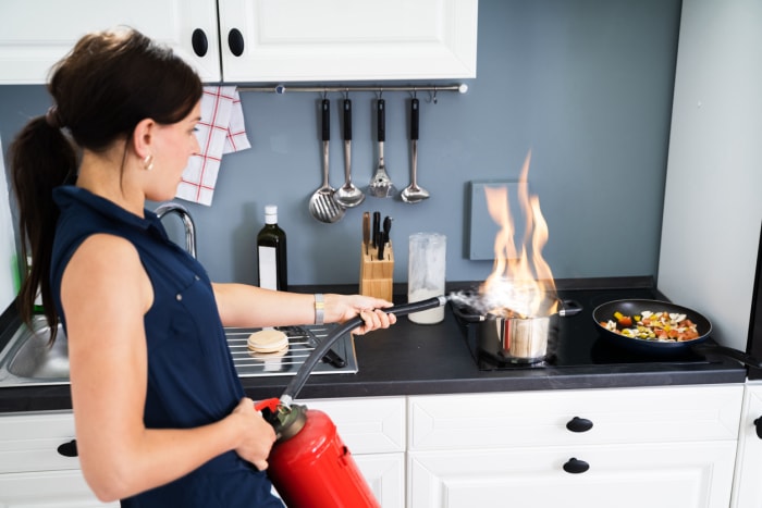 femme dans la cuisine utilisant un extincteur pour éteindre le feu dans une casserole sur la cuisinière