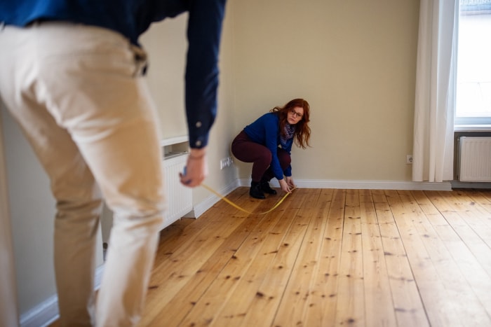 femme mesurant la superficie en pieds carrés d'une pièce pour déterminer la taille du mini-split nécessaire