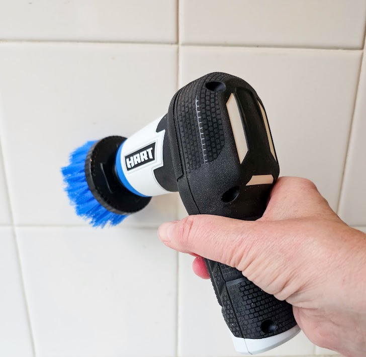 Une personne utilisant la brosse rechargeable Hart Tools 4V pour nettoyer les carreaux.