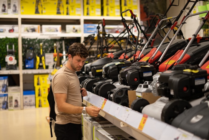 Man in casual clothes checking price of new lawn mower on tag while shopping in store of power tools