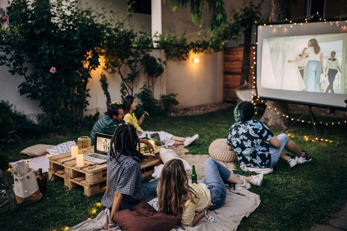 Des amis regardent un film sur le vidéoprojecteur dans le jardin