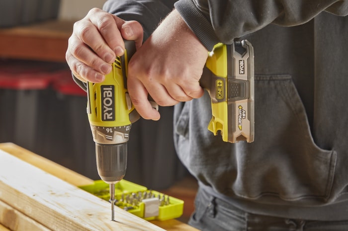 Un homme utilise une perceuse pour enfoncer une fixation dans une planche de bois.