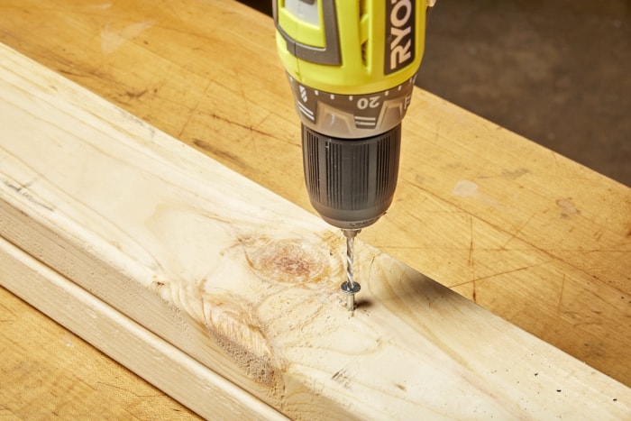 Une personne utilise une mèche à gauche pour retirer une vis dénudée d'un montant en bois dans un atelier domestique.