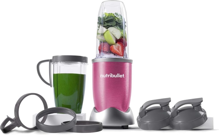 Un mixeur Nutribullet Pro 900 Watt rose baie se trouve à côté d'un smoothie vert et de divers couvercles.