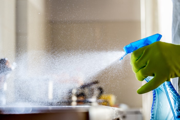 Une main gantée pulvérise un produit nettoyant bleu sur une surface de travail.