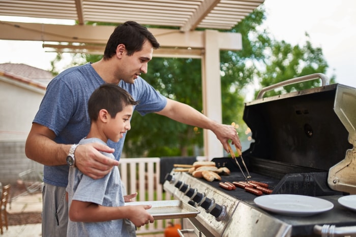 Un père apprend à son fils à faire des grillades sur un gril d'extérieur.