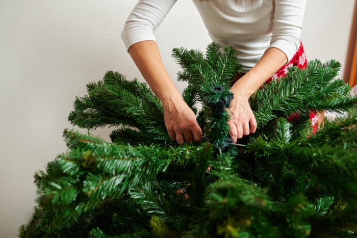 Une femme méconnaissable assemble un sapin de Noël artificiel dans son salon en pyjama de Noël