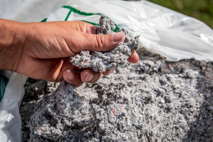 Une main tient un échantillon de cellulose soufflée au-dessus d'un sac rempli de celle-ci.